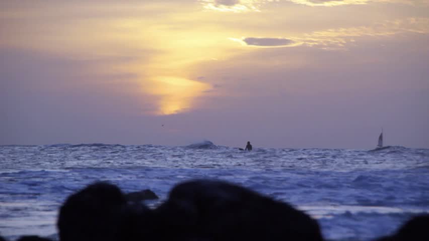 Surfers with a beautiful sunset and a sailboat