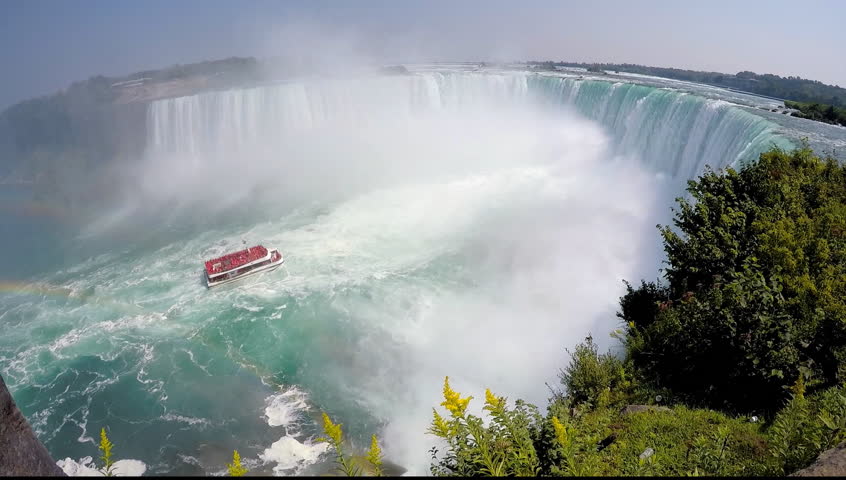 Catamaran tour boat with tourists in red raincoats going upstream of Niagara River towards Horseshoe Falls with rainbow