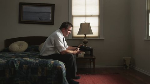 bored businessman passing the time in a hotel room looking at and smelling his shoe