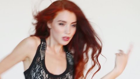 Woman with red hair dances in white studio. Close up view