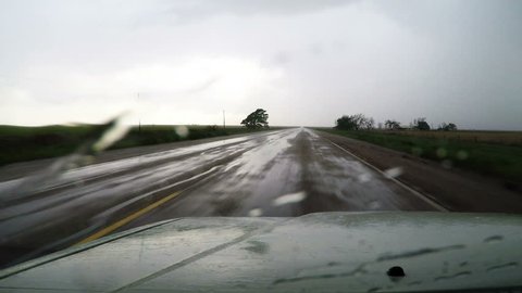 Point of view vehicle driving shot along a wet West Texas road in the rain. Windshield wiper wipes rain droplets quickly to improve visibility.