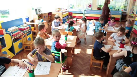 ST. PETERSBURG, RUSSIA - CIRCA MAY, 2015: Educators help children a pupils to drawing in daycare center at the skill lesson, preschool kids. Russian kindergarten is a preschool educational institution