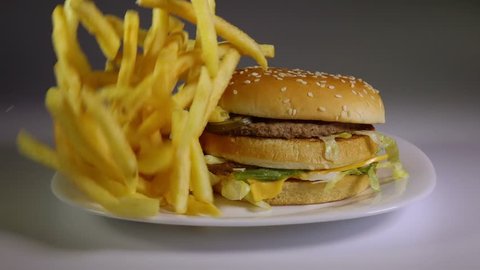 Fried potato chips falling down on hamburger, slow motion, fast food, junk food concept.