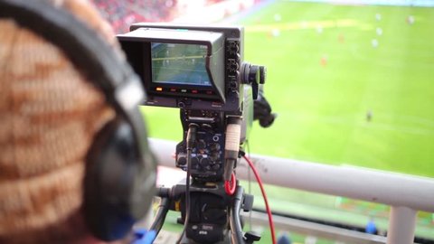 Cameraman shoots video reportage at stadium during game between soccer teams.