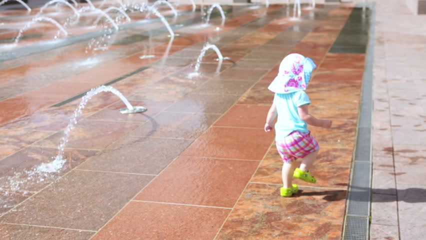 Cute toddler girl playing with small fountains in splash park.