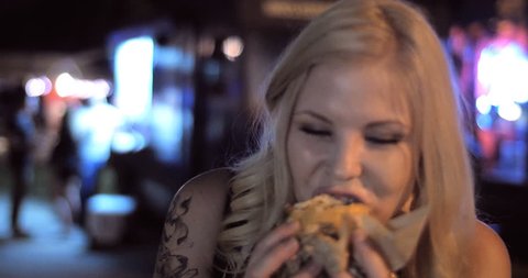 4K - A Close up shot of pretty hipster hip cool fun girl eating late night burger from a popular trendy food truck in a urban street festival setting at night.  Version 1 - shorter