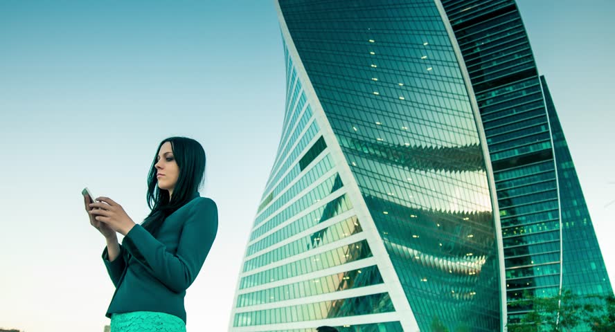 Business woman speaks on the phone on the background of skyscrapers.