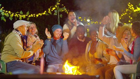 4K Happy mixed ethnicity group of friends socializing together outdoors in front of open fire. Shot on RED Epic.