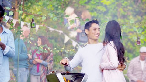 4K Happy attractive Asian couple cooking at bbq while friends socialize in the background. Shot on RED Epic.