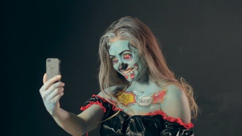 Girl in makeup of dreaded zombie making selfie on her phone in the studio