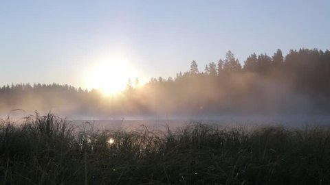 Locked-down shot of fog moving slowly at a calm lake during sunset in Finland.