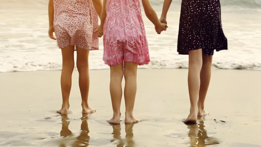 3 sisters standing on sea shore beach looking out at the ocean. Walk into the water
