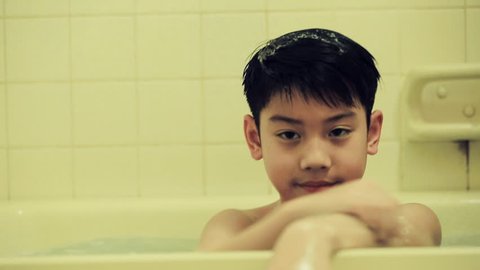 Little asian boy uses moisturizer in bathroom after having in bath