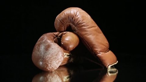 Old boxing gloves rotating on reflective surface.