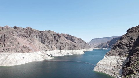 Hoover Dam hydroelectric and view of Lake Mead on Colorado River across mountain peaks and valley supporting the concrete structure. Very low water in lake and Colorado River. Pan across water.