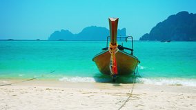 Video UltraHD - Handmade. wooden tour boat. tied on a pristine. white sand. tropical beach. bobbing in the gentle surf with other boat traffic in the background.