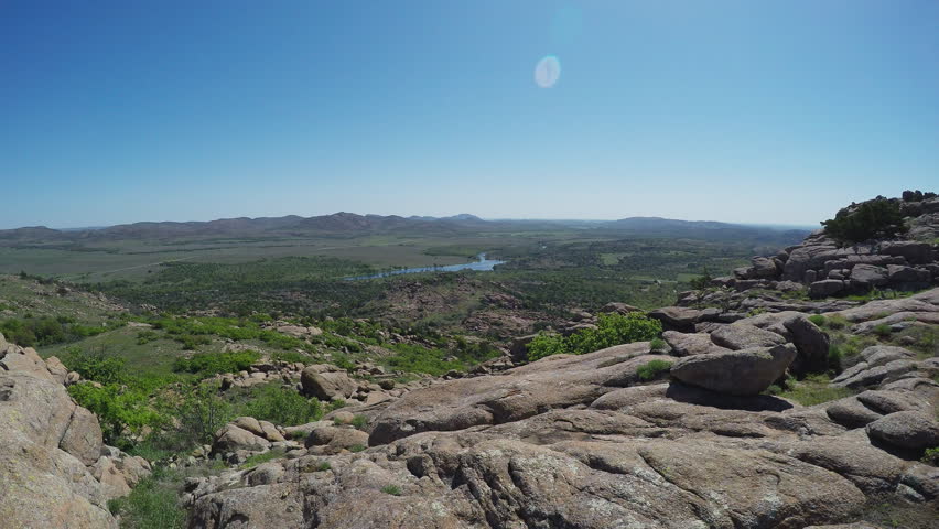 Wide shot of a scenic vista from the Wichita Mountain peak in Lawton Oklahoma in 4K format. Clip features a long distance view from a rocky mountain top of the green valley below.