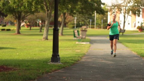 Dolly shot of female athlete running in beautiful park.