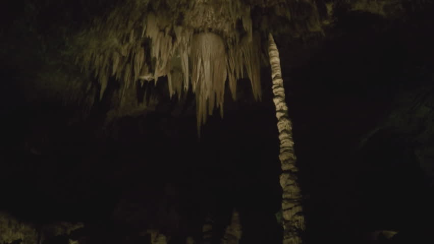 Shot of a group of stalactites hanging from ceiling at Carlsbad Caverns in New Mexico. A very tall stalagmite reaches up and nearly touches cave ceiling high above.