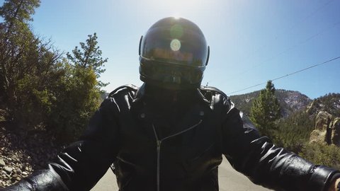 Close up shot of a backlit helmeted motorcycle rider on a mountain highway in 4k format. The sun shines down on a biker riding on a rural back road.