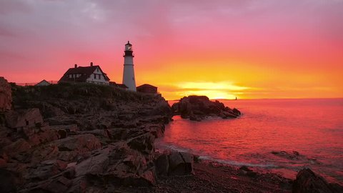 Establishing aerial shot of a gorgeous sunrise in Maine capturing a Lighthouse. Vivid colors of purples, pinks and yellows are reflected in the water.