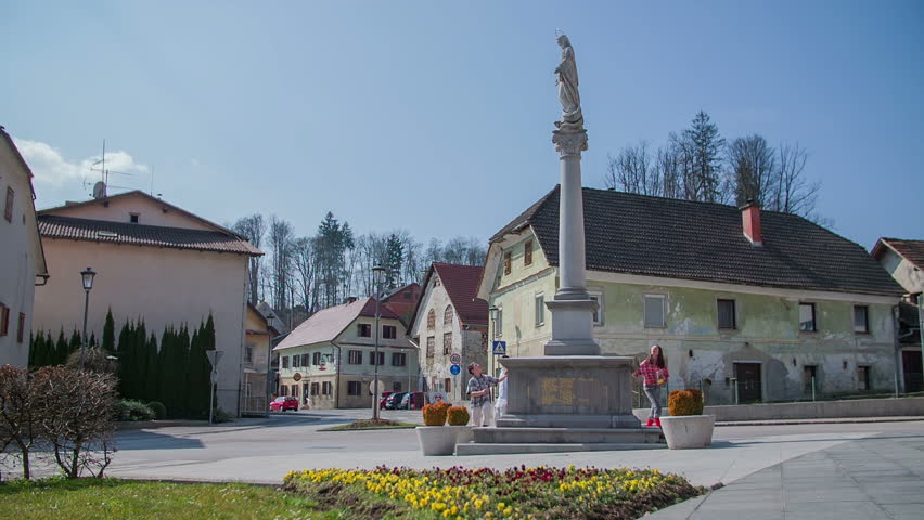 Group of young children walking on the square with a statue in the countryside, footage is taken in slow motion.