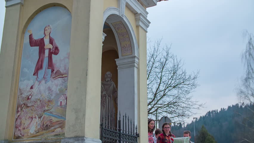 Group of children comes to the chapel in the middle of the village with a map in there hands, footage is taken in slow motion.