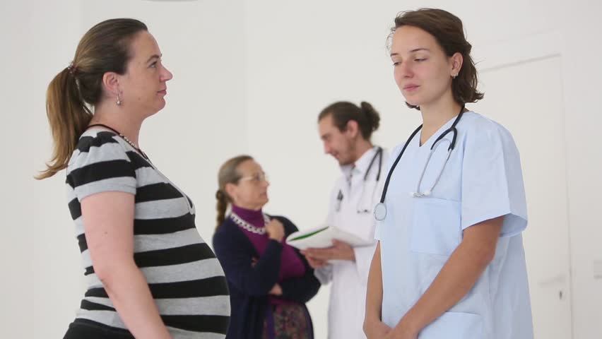 Pregnant woman talking with young obstetrician. On the background a doctor speaking with another woman Royalty-Free Stock Footage #11678786