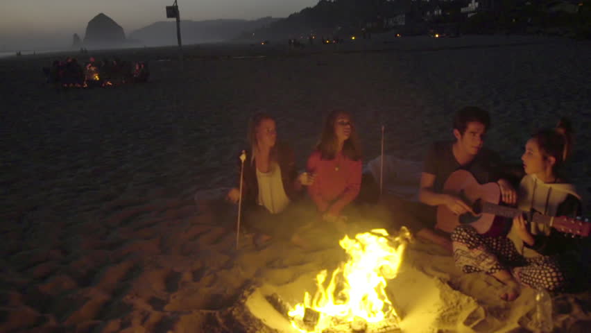 Wide shot of a group of friends listening to the guitar at the beach