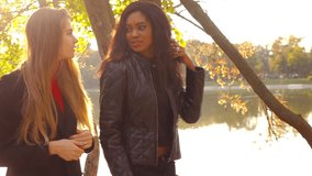 Two friends, young pretty girls, caucasian and african, having fun outdoors, walking, talking, laighing, slow motion.