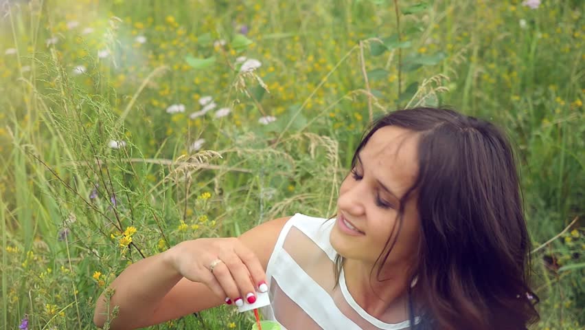 Slowmotion of Romantic beautiful young smiles woman blowing soap balloons in a flower meadow. 1920x1080