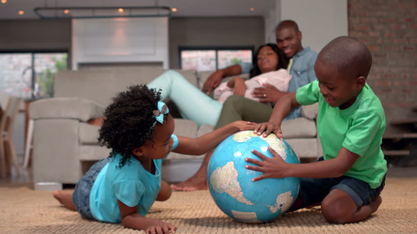 Siblings looking at globe on the floor while parents watch in slow motion