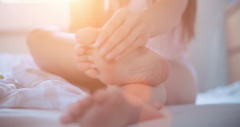 Woman applying cosmetic foot cream, doing feet massage, close up. Slow Motion 120 fps, 4K, DCi. SPA at home. Cozy healthy comfortable living. Lens Flare. Young woman using feet moisturizer, skin care.