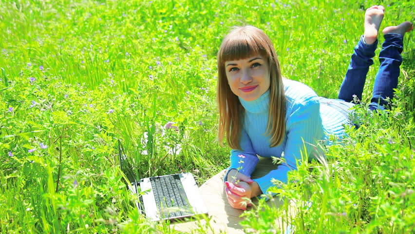 Beautiful woman lying in a meadow near a laptop. Look at camera. 