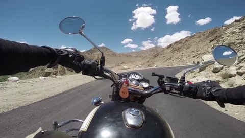 Driver riding on motorcycle on high mountain winding road following friends on motorbikes