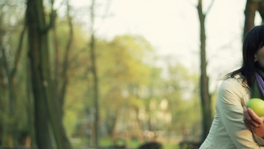 Young happy woman with flower and apple in the park, dolly shot 