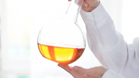 Scientist mixing Volumetric flask with yellow liquid in laboratory