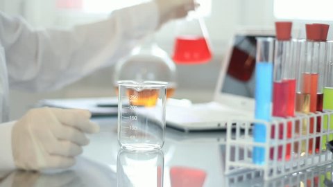 Scientist in protective gloves filling the beakers with different liquid