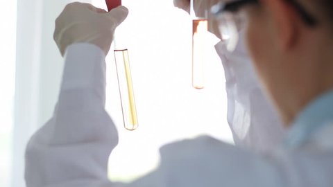 Rear view of female scientist holding two test tubes with yellow substance