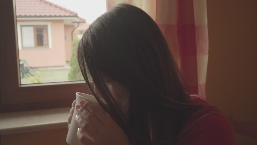 Woman drinking tea or coffee indoor, alone sad girl long hair looking dreaming through window holds mug with hot beverage at home.4K | Shutterstock HD Video #11735165