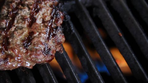 A hamburger on a gas grill with open flames is flipped with a metal spatula. Excellent text-friendly space. Shot in 1920x1080 HD widescreen size.