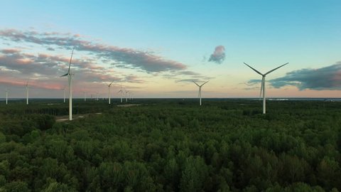Aerial drone shot of wind turbines in the forest near the sea at sunset. Shot in 4K (UHD).