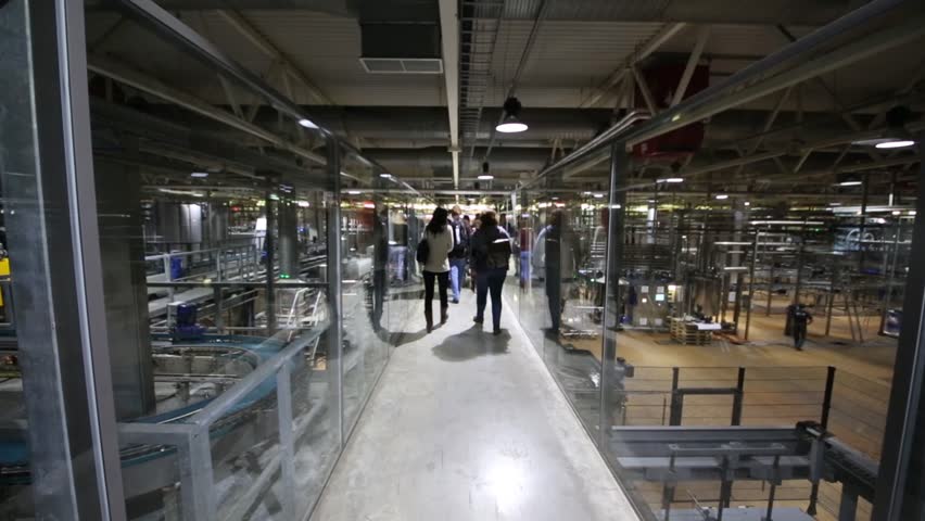 People go in glass hallway in workshop of modern big brewery