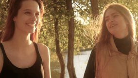 Two friends, young pretty girls, caucasians, having fun outdoors in park, walking, talking, laughing, fooling around, slow motion.