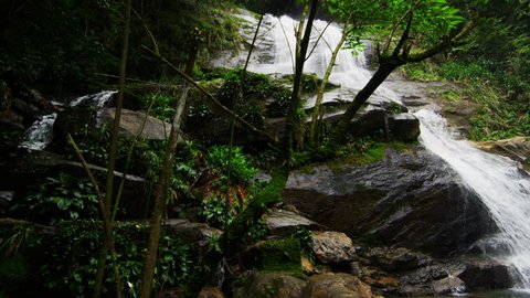 RIO DE JANEIRO - CIRCA JUNE 2013: Tracking shot of a jungle waterfall cascading down a rocky escarpment into a deep green pool at the bottom. Tijuca National Park. Filmed June 24, 2013.