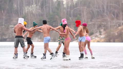 Eight people in underwear round dance on natural ice rink at winter