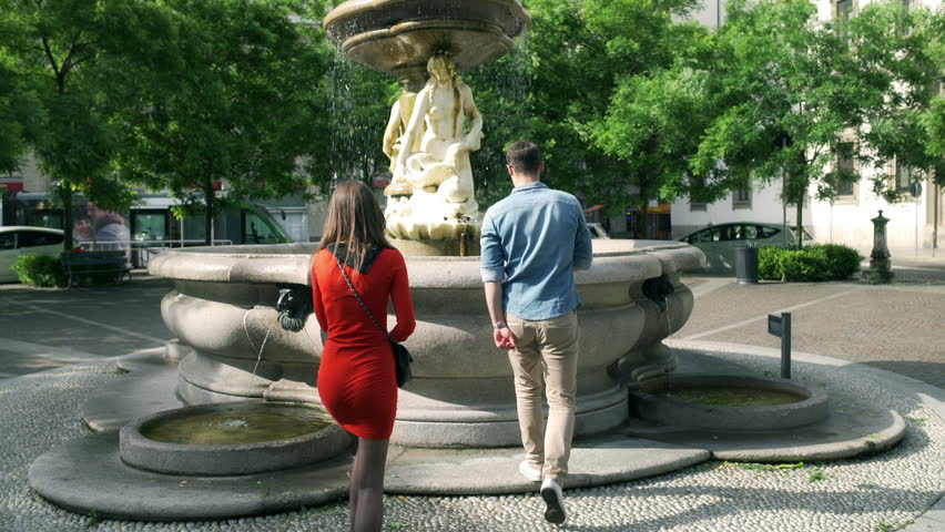Couple standing next to the fountain and using smartphone, steadycam shot
