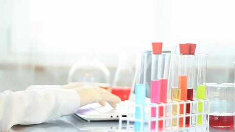 Female scientist examine test tubes with chemicals and writing results on laptop