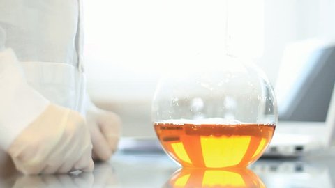 Female scientist looking at volumetric flask with yellow substance, camera stabilizer shot
