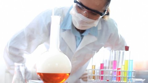 Female scientist examines smoky Volumetric Flask with yellow liquid